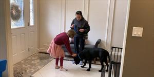 Woman watches girl give black dog a treat